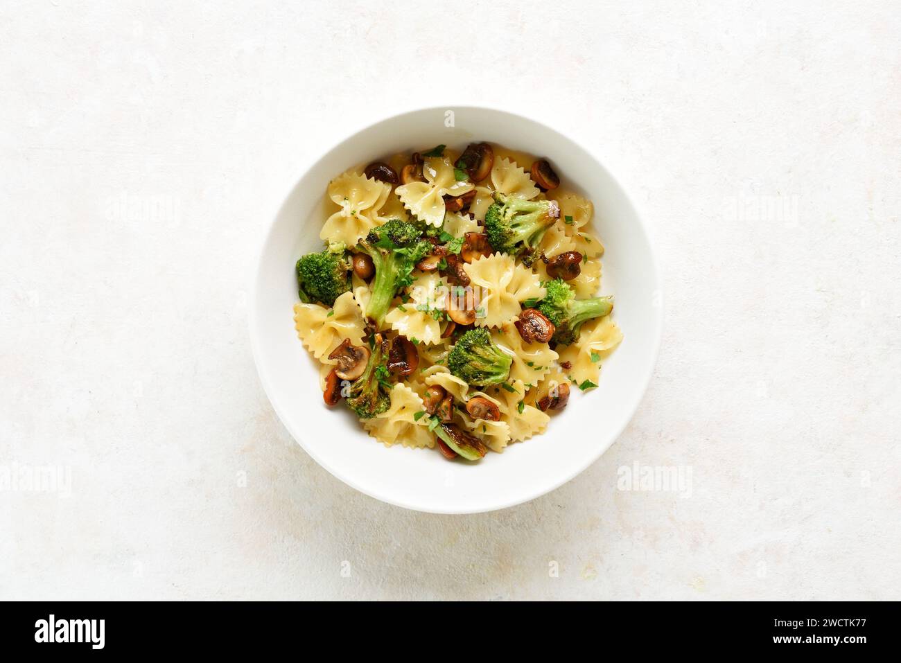 Farfalle con broccoli arrostiti e funghi in ciotola su sfondo bianco con spazio per la copia. Piatto di farfalle preparato in casa con arrosto Foto Stock