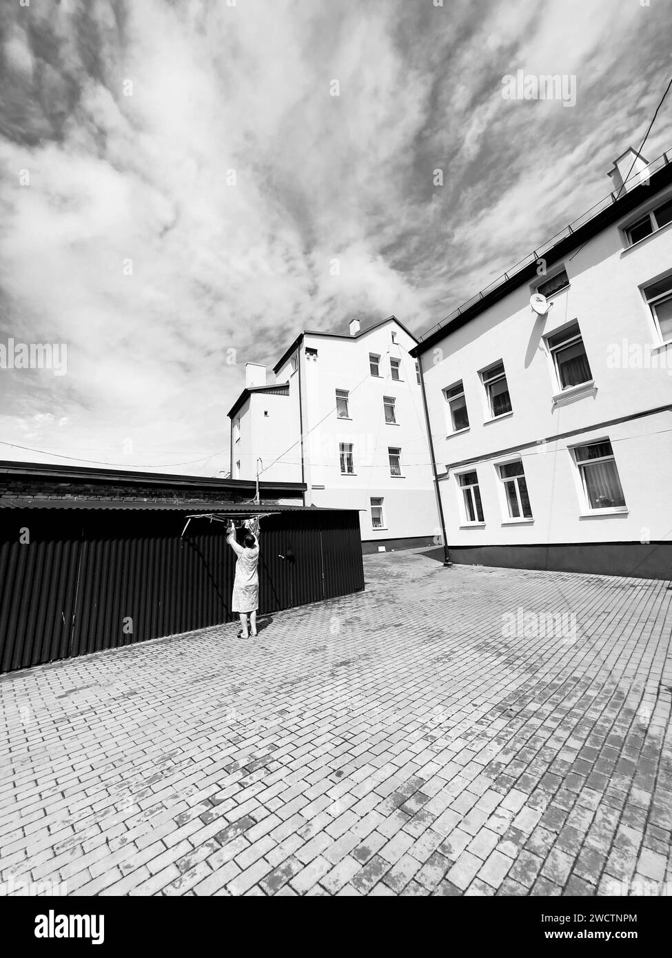 la donna appende la lavanderia fuori da un modesto edificio in una città provinciale, lastricata di ciottoli sotto un vasto cielo Foto Stock