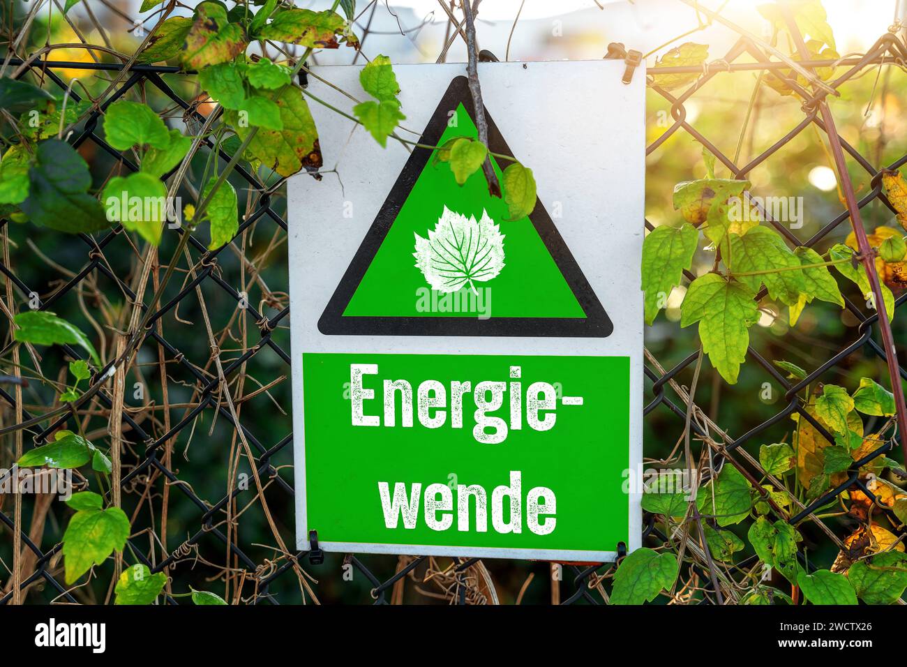 16 gennaio 2024: Cartello verde su una recinzione circondata da foglie verdi con l'iscrizione: Energiewende FOTOMONTAGE *** Grünes Schild an einem Zaun umgeben von Grünen Blättern mit der Aufschrift: Energiewende FOTOMONTAGE Foto Stock