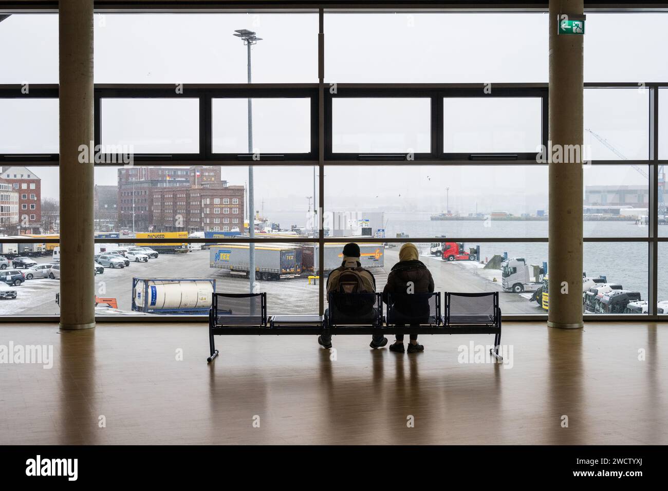 Ein Mann und eine Frau auf einer Sitzbank im Terminalgebäude der Stena Line auf das Panorama des Kieler Hafens blickend Foto Stock