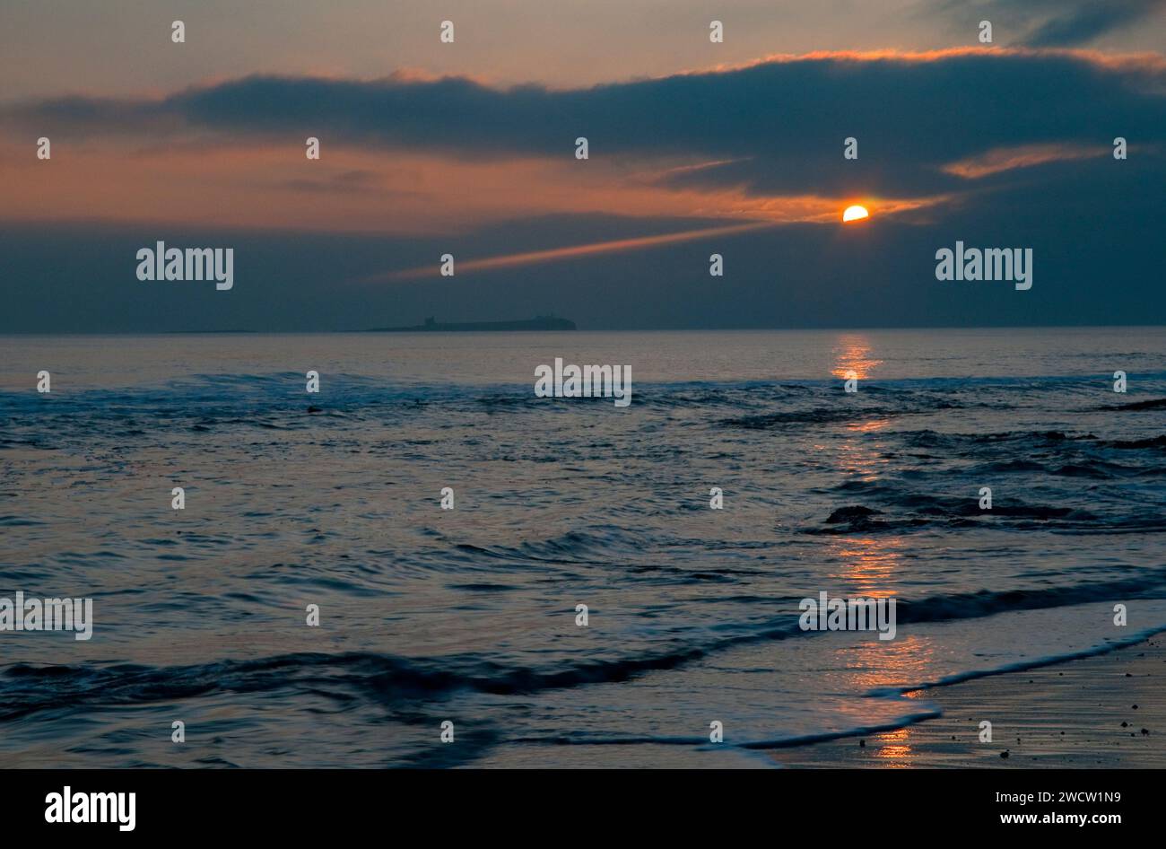 Affacciato sul mare dalla costa di Bamburgh Beach la mattina presto di marzo, con il sole al tramonto e il sentiero arancione che attraversa il Mare del Nord Foto Stock