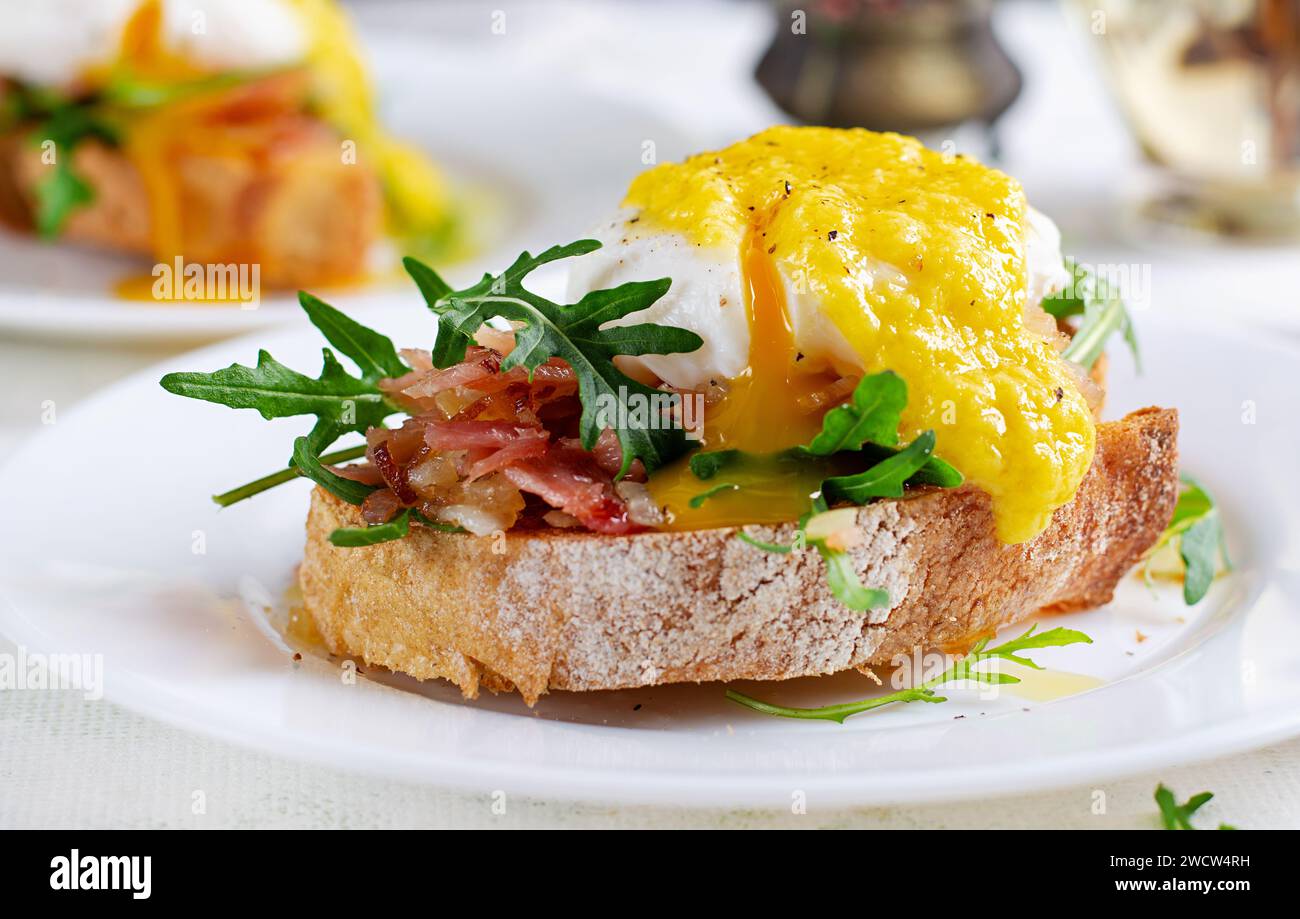 Colazione. Sandwich con prosciutto, uovo in camicia, cipolla e rucola in un piatto su sfondo chiaro Foto Stock
