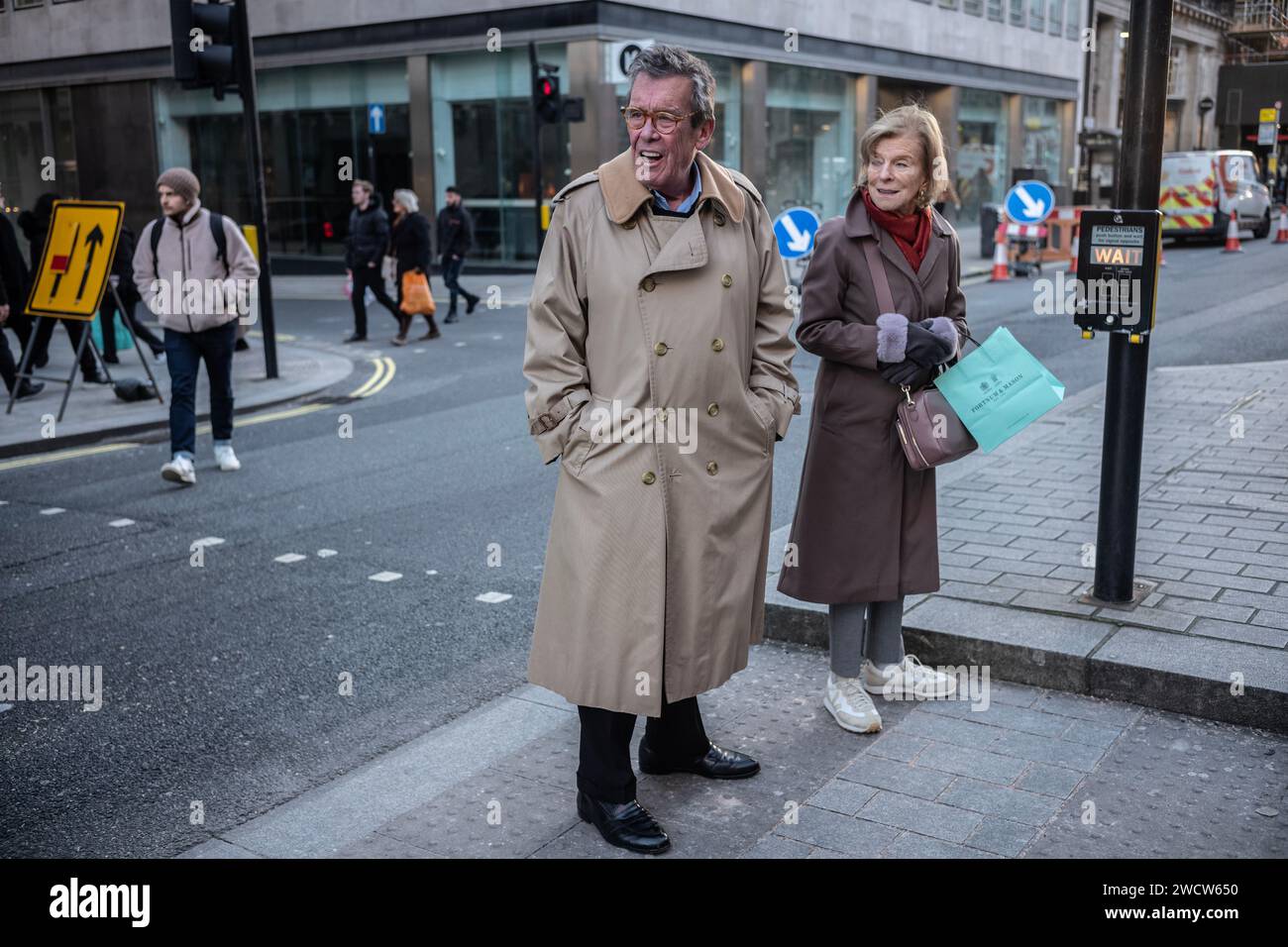 Un uomo con un impermeabile invernale si trova ad un passaggio pedonale per controllare che la strada sia libera da attraversare, Piccadilly, Londra, Inghilterra, Regno Unito Foto Stock