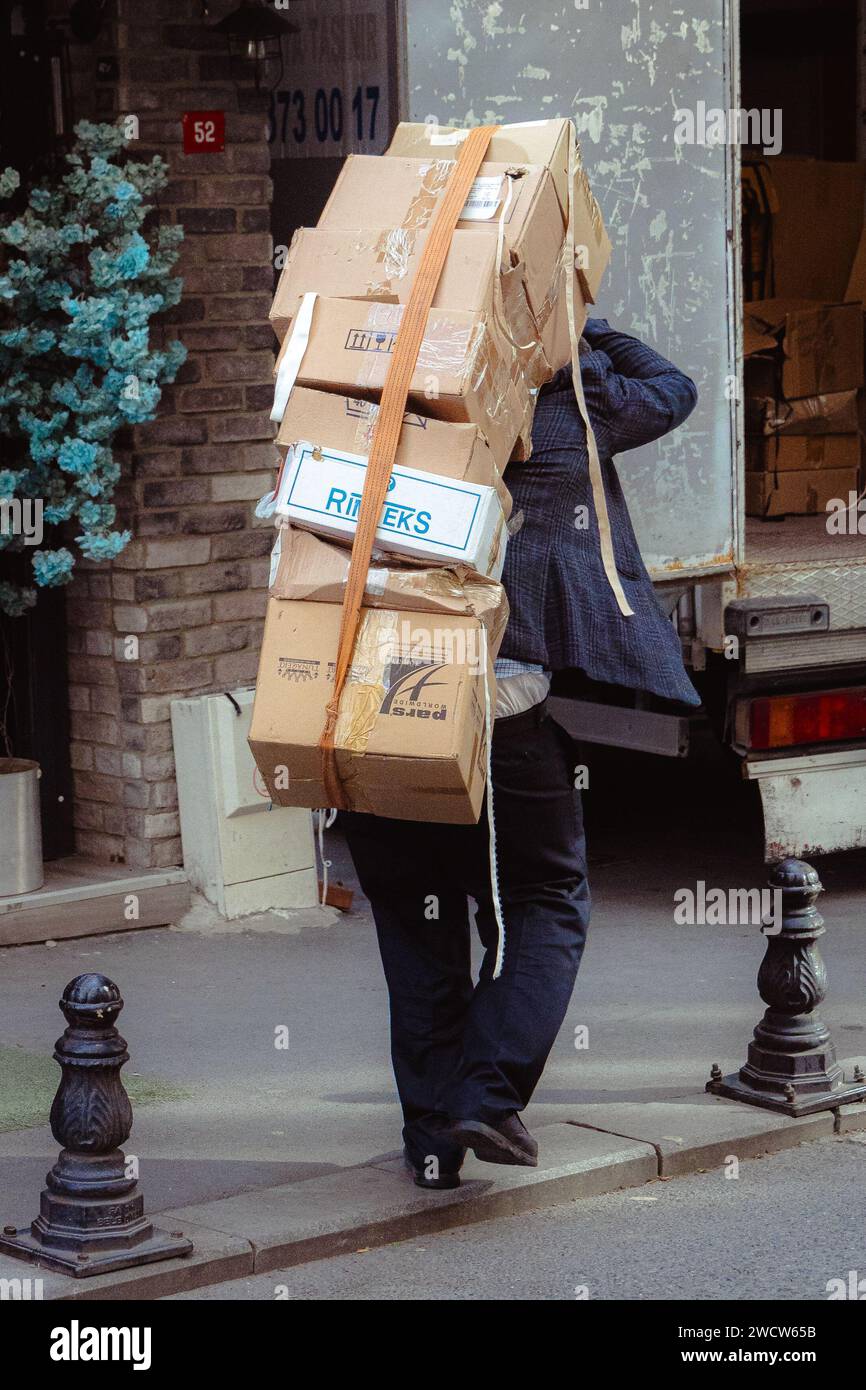 Un uomo turco che trasporta un pesante carico di scatole sulla schiena attraverso le strade di Istanbul, conosciuto come hamal o porter a Istanbul, in Turchia Foto Stock