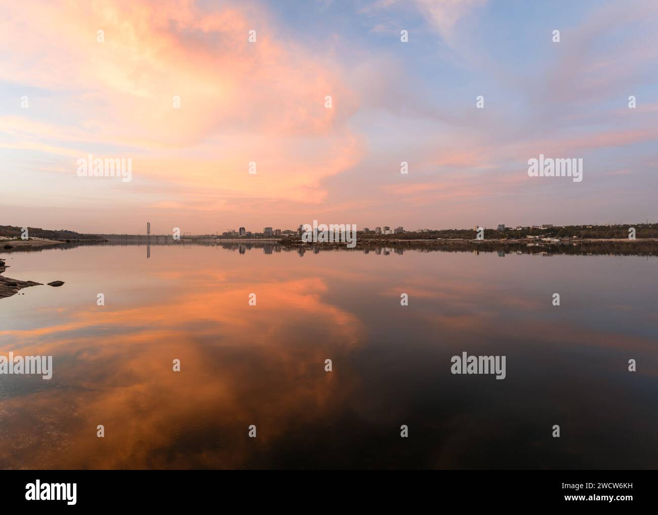 Paesaggio urbano durante il tramonto sulla riva di un ampio fiume in cui si riflette il cielo. Contesto Foto Stock Paesaggio urbano durante il tramonto sulla riva di un ampio fiume in cui si riflette il cielo. Contesto Foto Stock