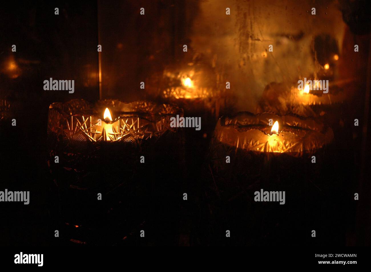 Le fiamme scintillanti di candele commemorative che bruciano su una sporgenza di pietra creano una calda e lunatica atmosfera arancione. Foto Stock