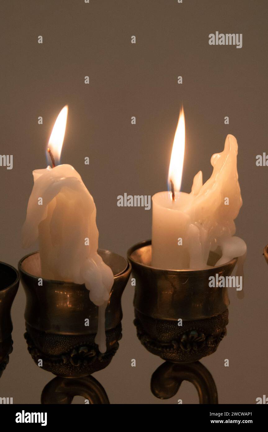 Due candele fonse a cera conica che bruciano in tazze d'argento opacizzate di un candelabro. Foto Stock