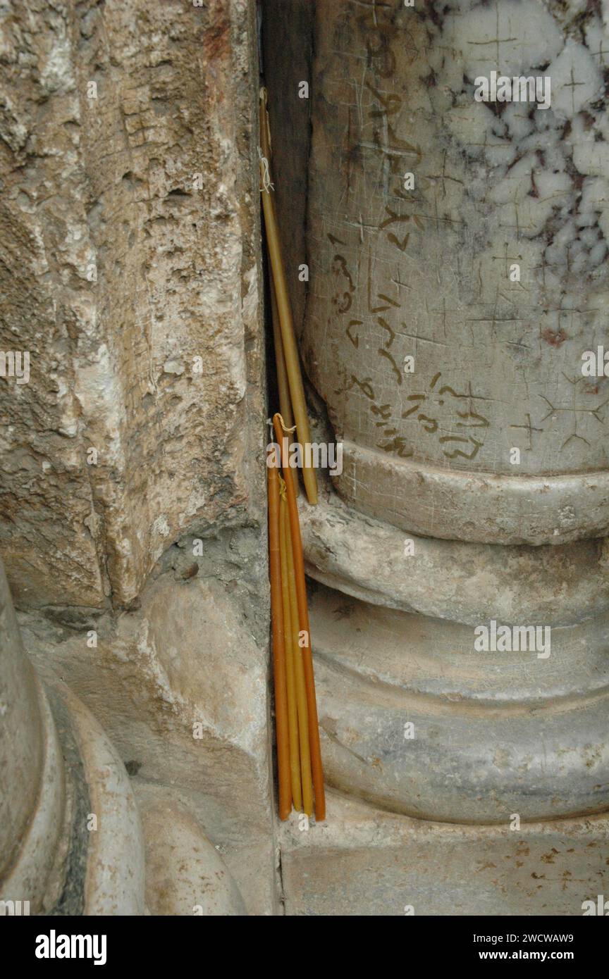 Candele votive gialle, cerate e gialle giacciono in una cranny di colonne di pietra fuori dalla Chiesa del Santo Sepolcro a Gerusalemme la domenica di Pasqua. Foto Stock