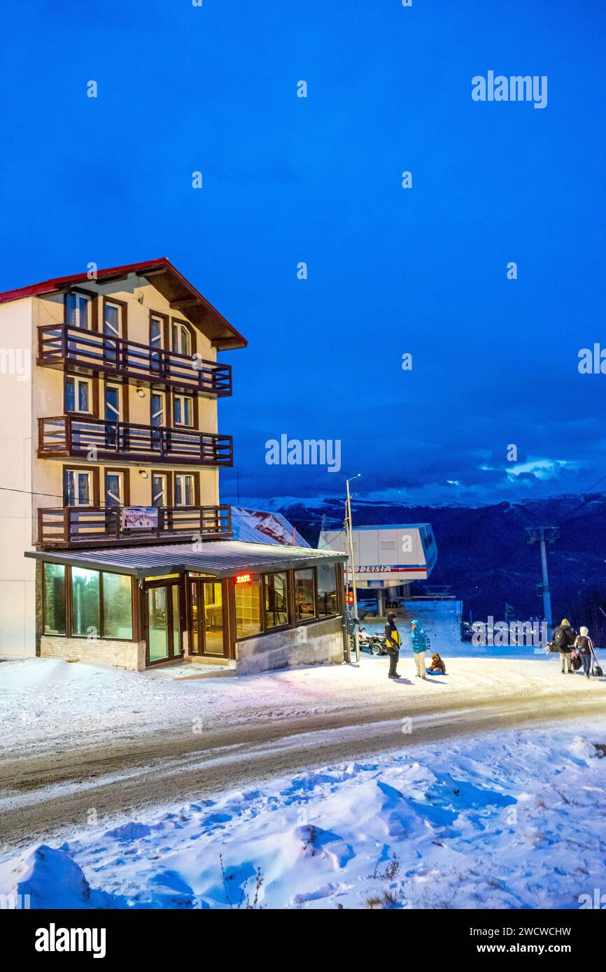 Un gruppo di persone che passeggiano all'esterno di un magnifico edificio, godendosi il paesaggio notturno con una vista mozzafiato delle piste da sci innevate. Foto Stock