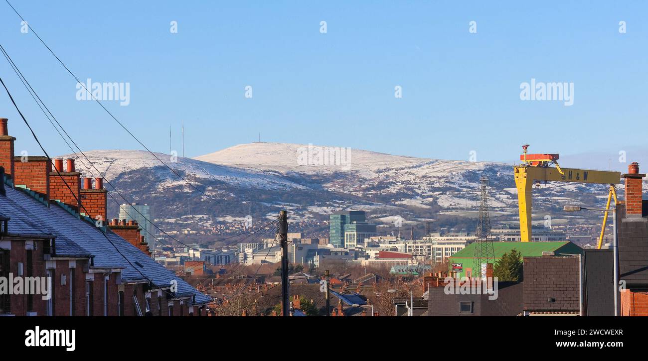 Belfast, Irlanda del Nord, Regno Unito. 17 gennaio 2024. Clima britannico - sole invernale brillante dopo il brutto gelo e il ghiaccio di ieri sera, neve sulle colline di Belfast su Divis e Black Mountain, vista attraverso la Belfast industriale dal lato orientale della città. Credito: CAZIMB/Alamy Live News. Foto Stock