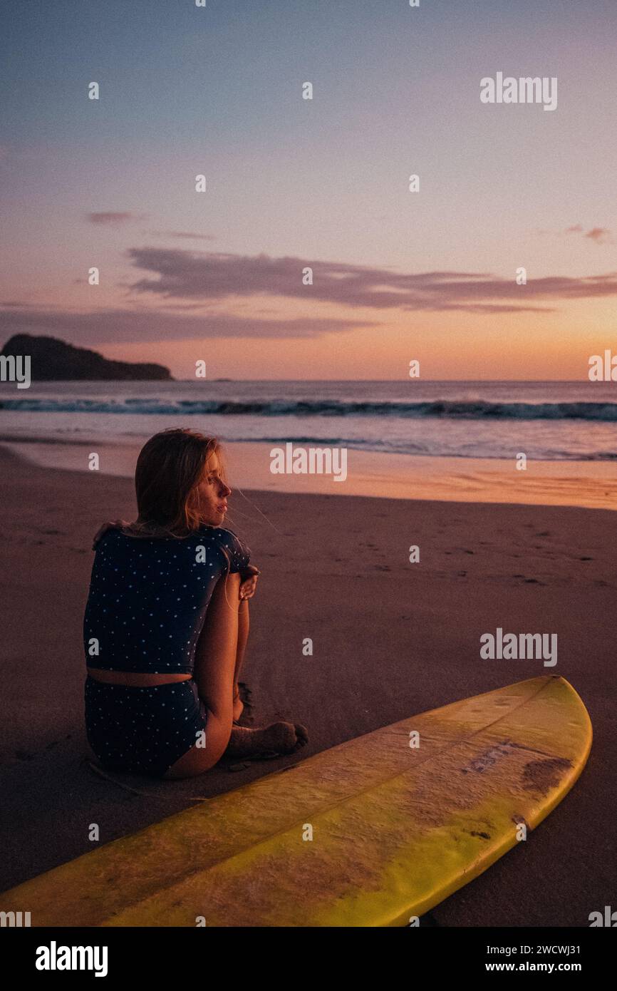 Una surfista che si rilassa su una spiaggia durante un tramonto Foto Stock