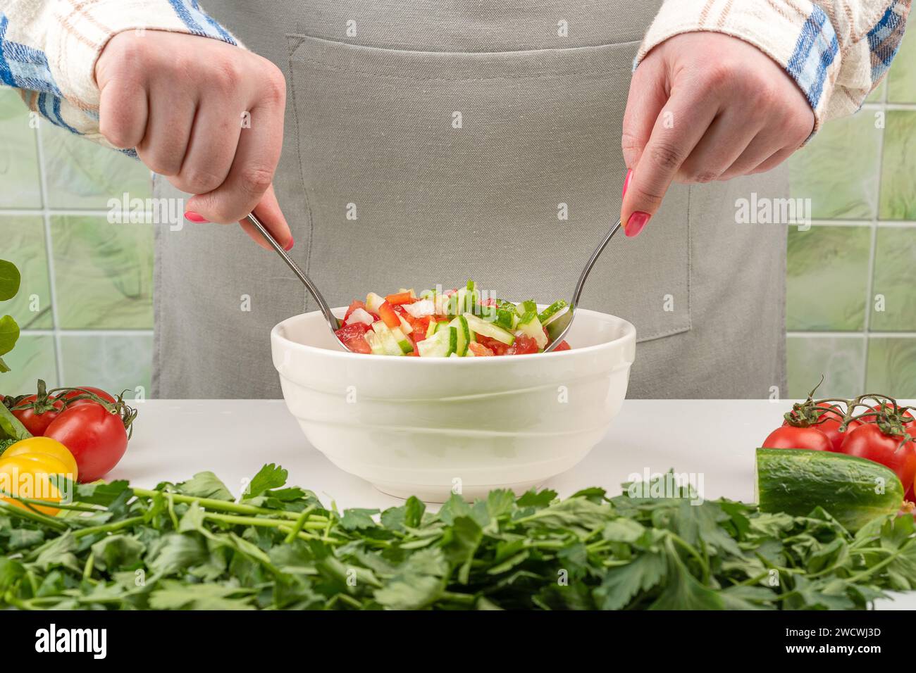 Una giovane donna mescola l'insalata con i cucchiai. Cucina casalinga. Foto Stock