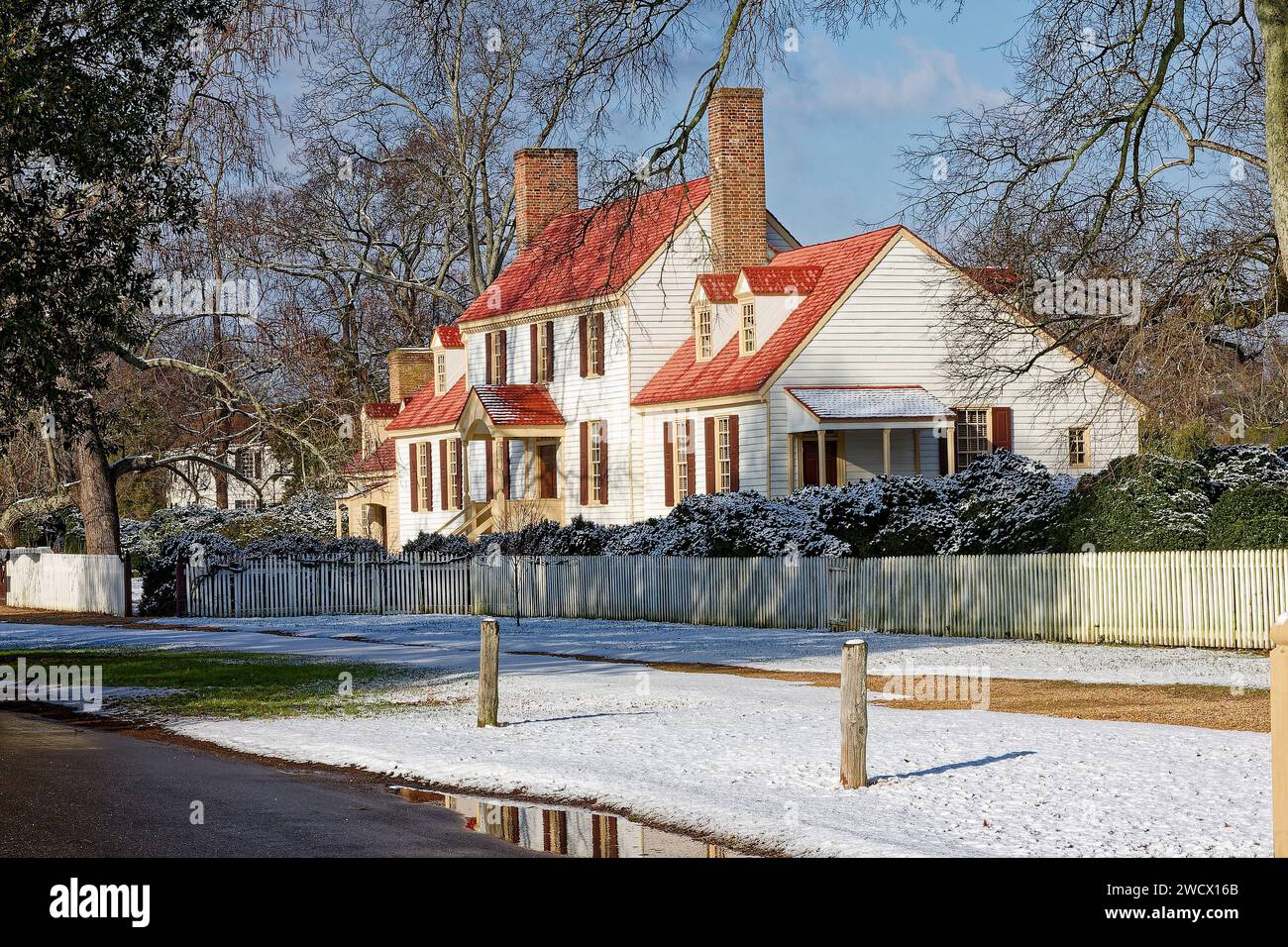 casa, cornice bianca, tetto rosso-arancione, persiane, stile coloniale, recinzione per picchetti, 2 camini in mattoni, arbusti, alberi, neve, Winter, Williamsburg; va Foto Stock
