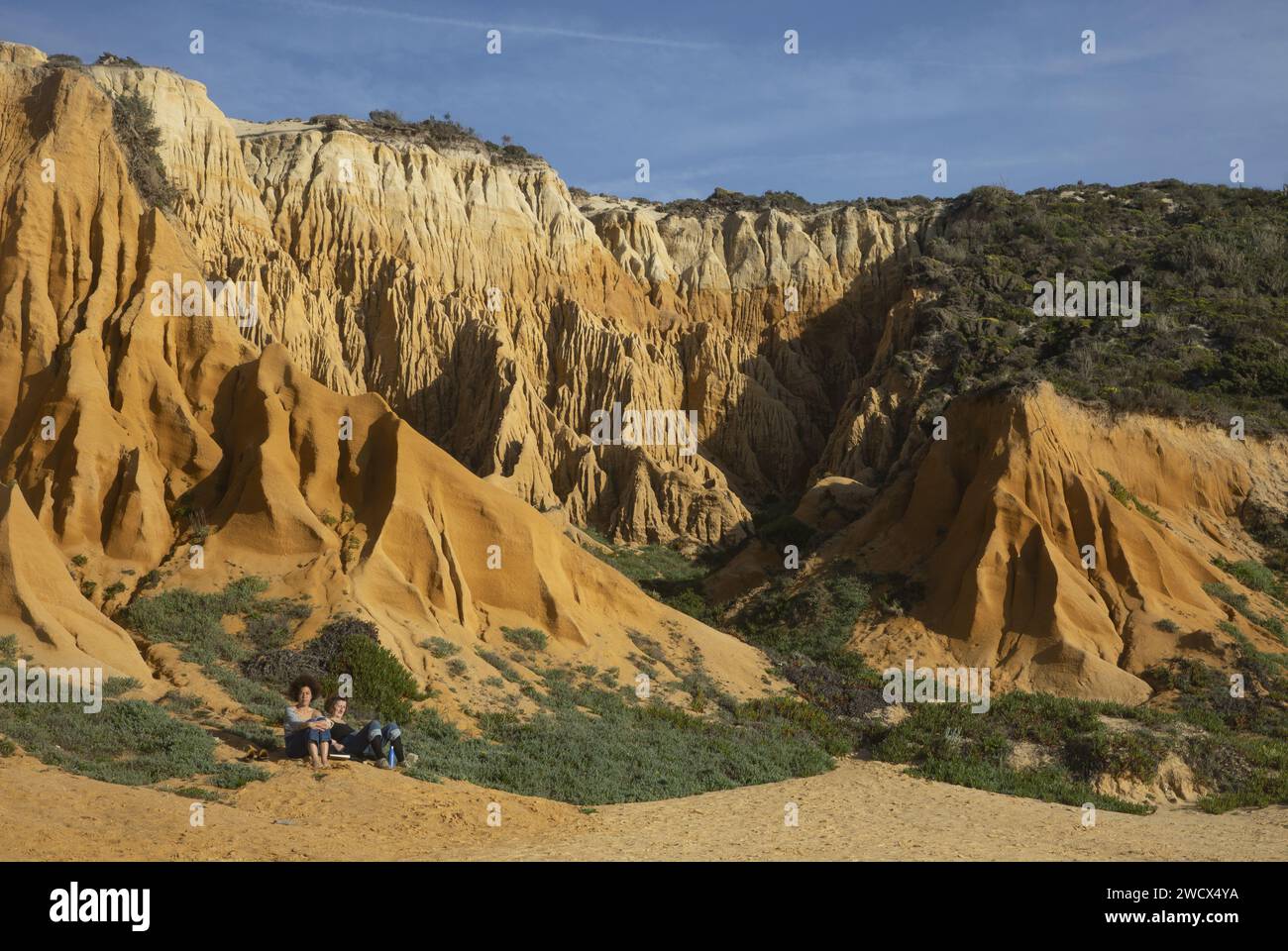 Portogallo, Alentejo, spiaggia di Gale Fontainhas, donne sedute ai piedi delle scogliere fossili ocra risalenti a cinque milioni di anni fa Foto Stock