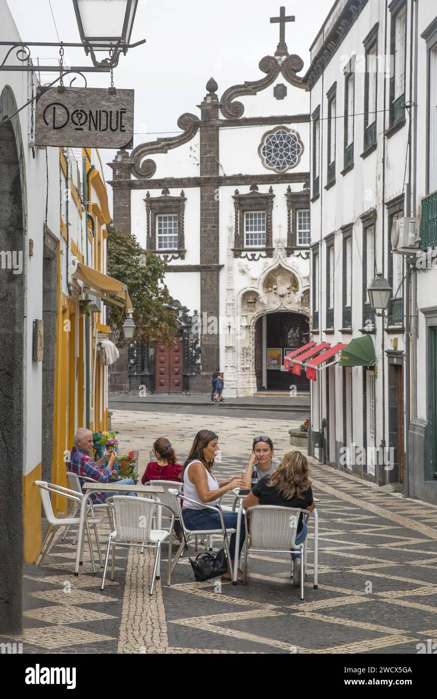 Portogallo, arcipelago delle Azzorre, isola di Sao Miguel, Ponta Delgada, persone sulla terrazza di un caffè in un vicolo con ciottoli bianchi e neri, di fronte a una chiesa barocca Foto Stock