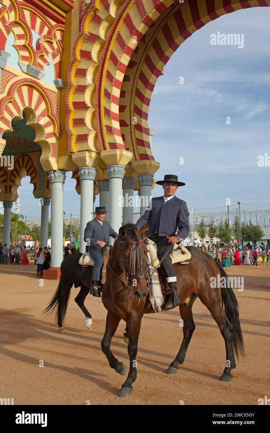 Spagna, Andalusia, Cordova, cavalieri in costume tradizionale a cavallo di fronte alla monumentale porta d'ingresso gialla e rossa della feria de Nuestra señora de la salud Foto Stock