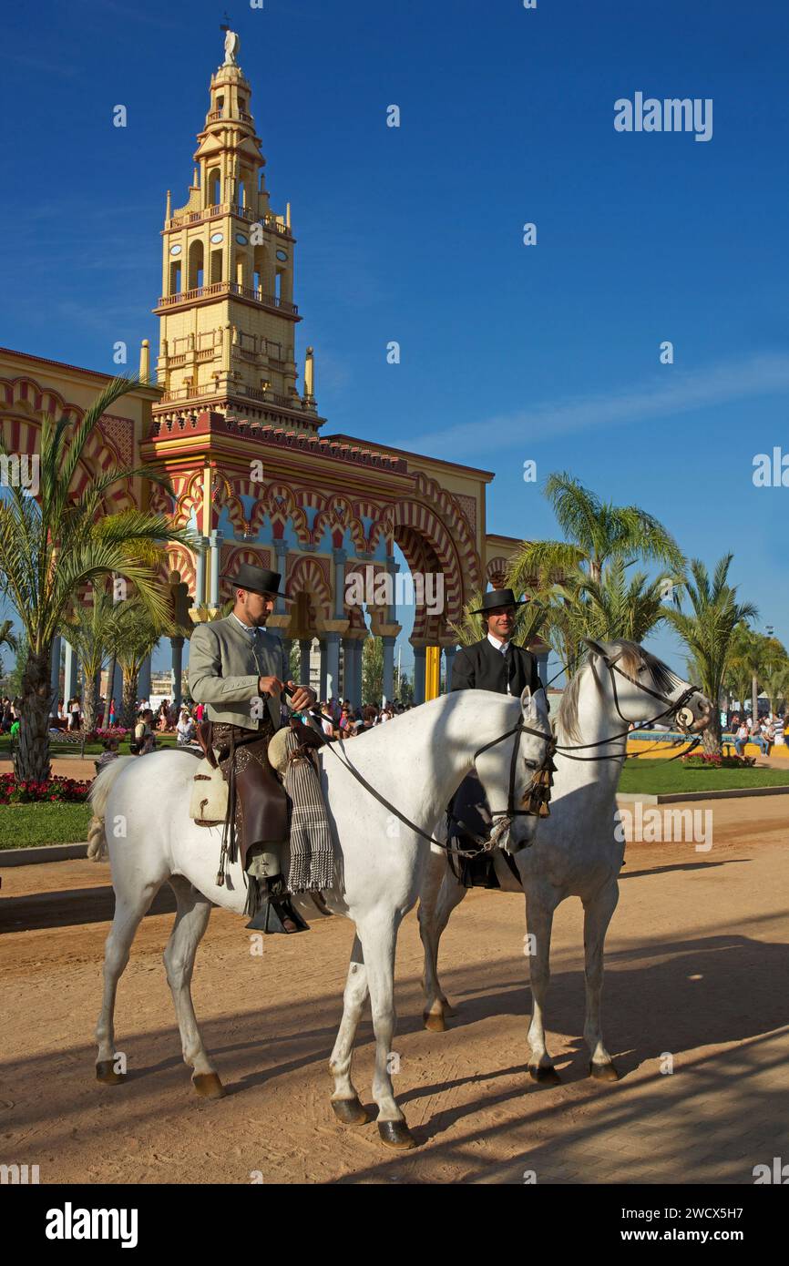 Spagna, Andalusia, Cordova, cavalieri in costume tradizionale a cavallo di fronte alla monumentale porta d'ingresso gialla e rossa della feria de Nuestra señora de la salud Foto Stock