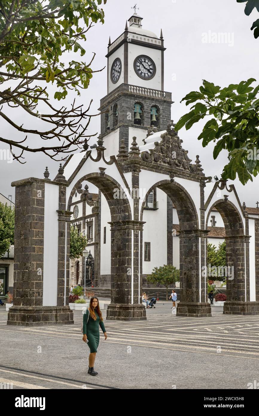 Portogallo, arcipelago delle Azzorre, isola di Sao Miguel, Ponta Delgada, giovane donna che cammina di fronte alle porte della città in pietra di basalto Foto Stock