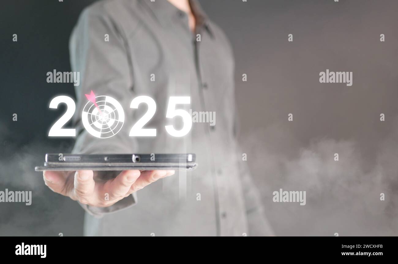 Buon anno 2025. Un uomo ha un tablet con un anno che cambia nel 2025, con un tabellone per fissare e concentrarsi sul nuovo obiettivo per il prossimo anno. Foto Stock