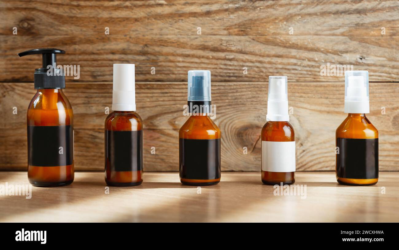 Set di bottiglie in vetro ambrato scuro con etichette vuote per cosmetici su sfondo di legno. Foto Stock