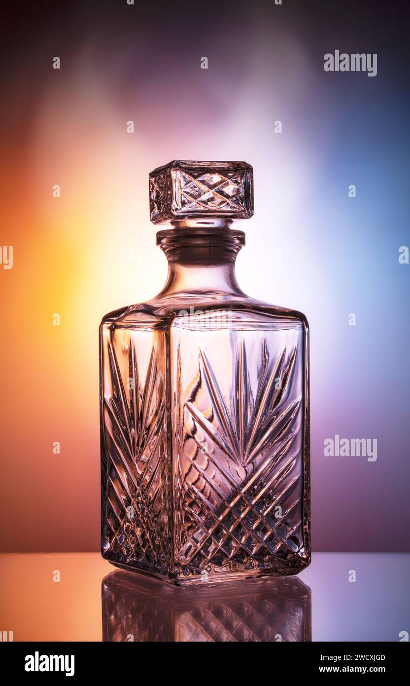 Decanter vuoto per whisky su sfondo blu-arancione. I colori si fondono perfettamente con un effetto foschia. Foto Stock