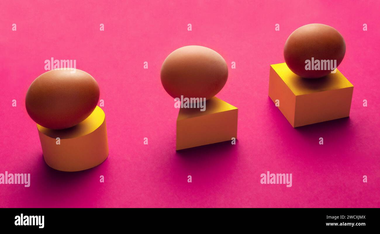 Composizione creativa e minimale di tre uova adagiate su un cilindro giallo, triangolo e cubo su sfondo viola. Foto Stock