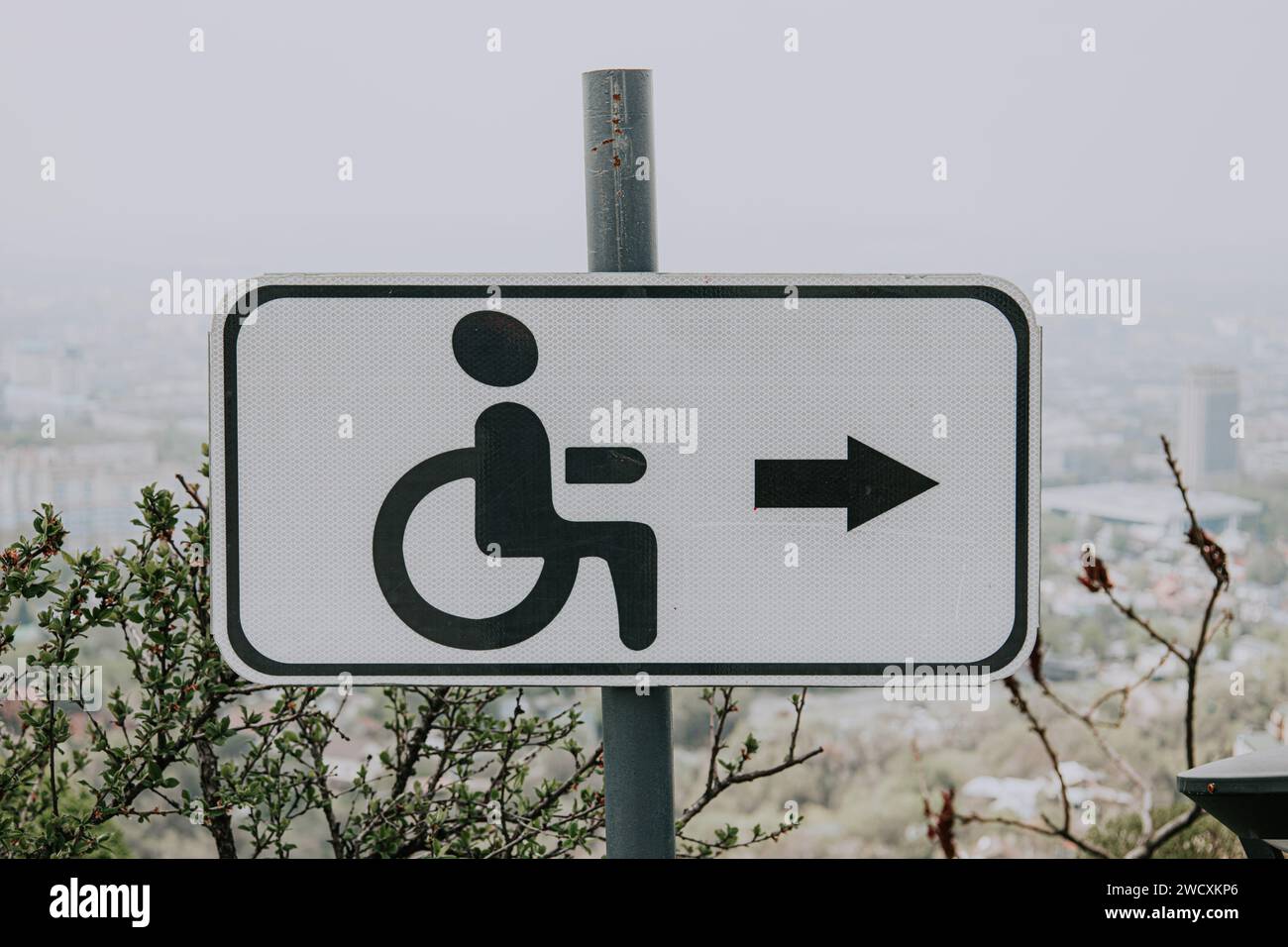 Cartello stradale bianco per disabili, disabili, con icona nera uomo in sedia a rotelle e freccia destra. Ambiente accessibile in spazi urbani. Foto Stock