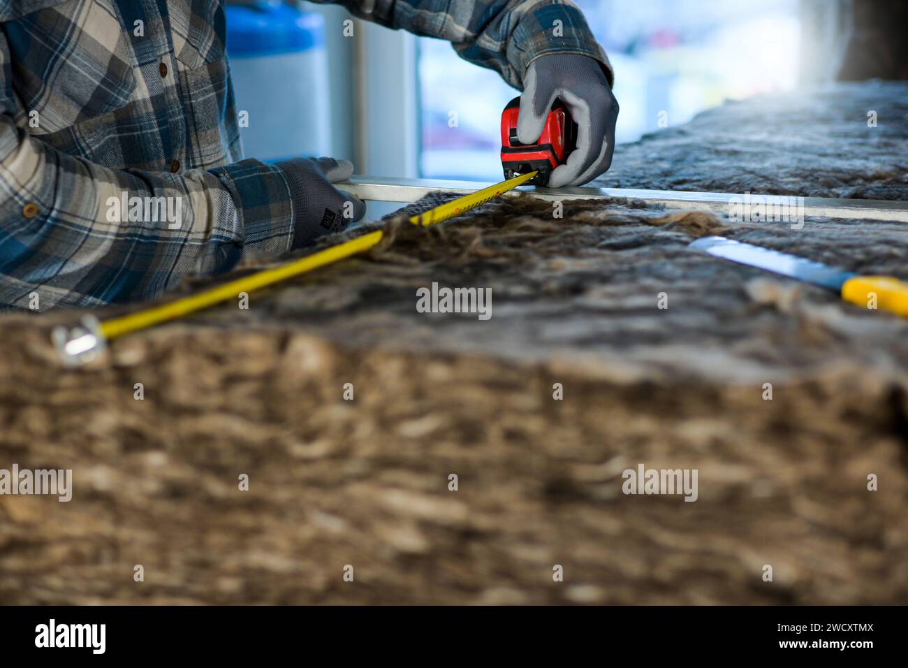 un lavoratore che indossa tute e guanti misura la lunghezza della lana di vetro con un metro. Foto Stock
