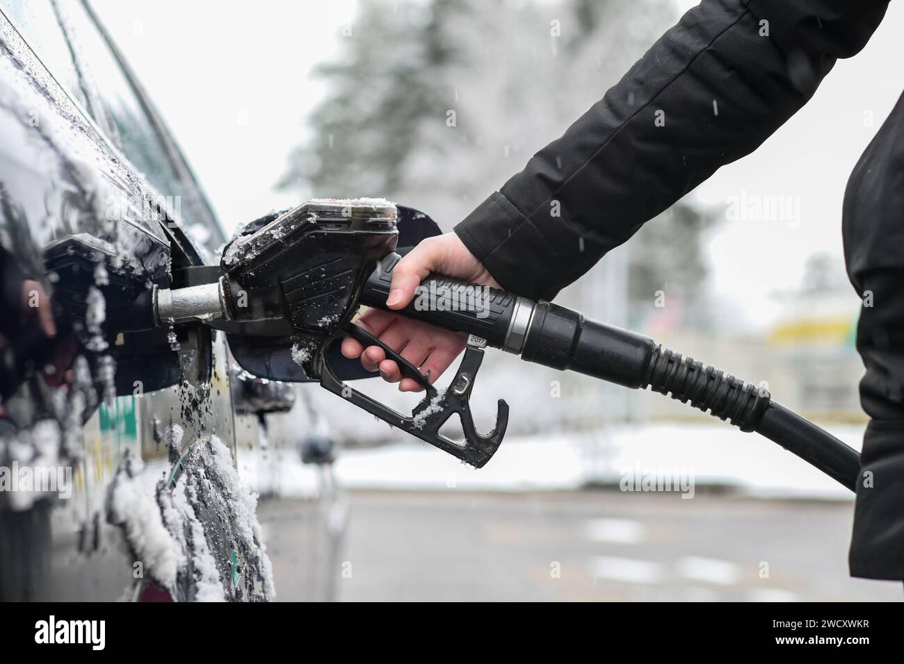 donna che tiene in mano una pistola per il rifornimento di un'auto ghiacciata in inverno e sfondo sfocato. Foto Stock