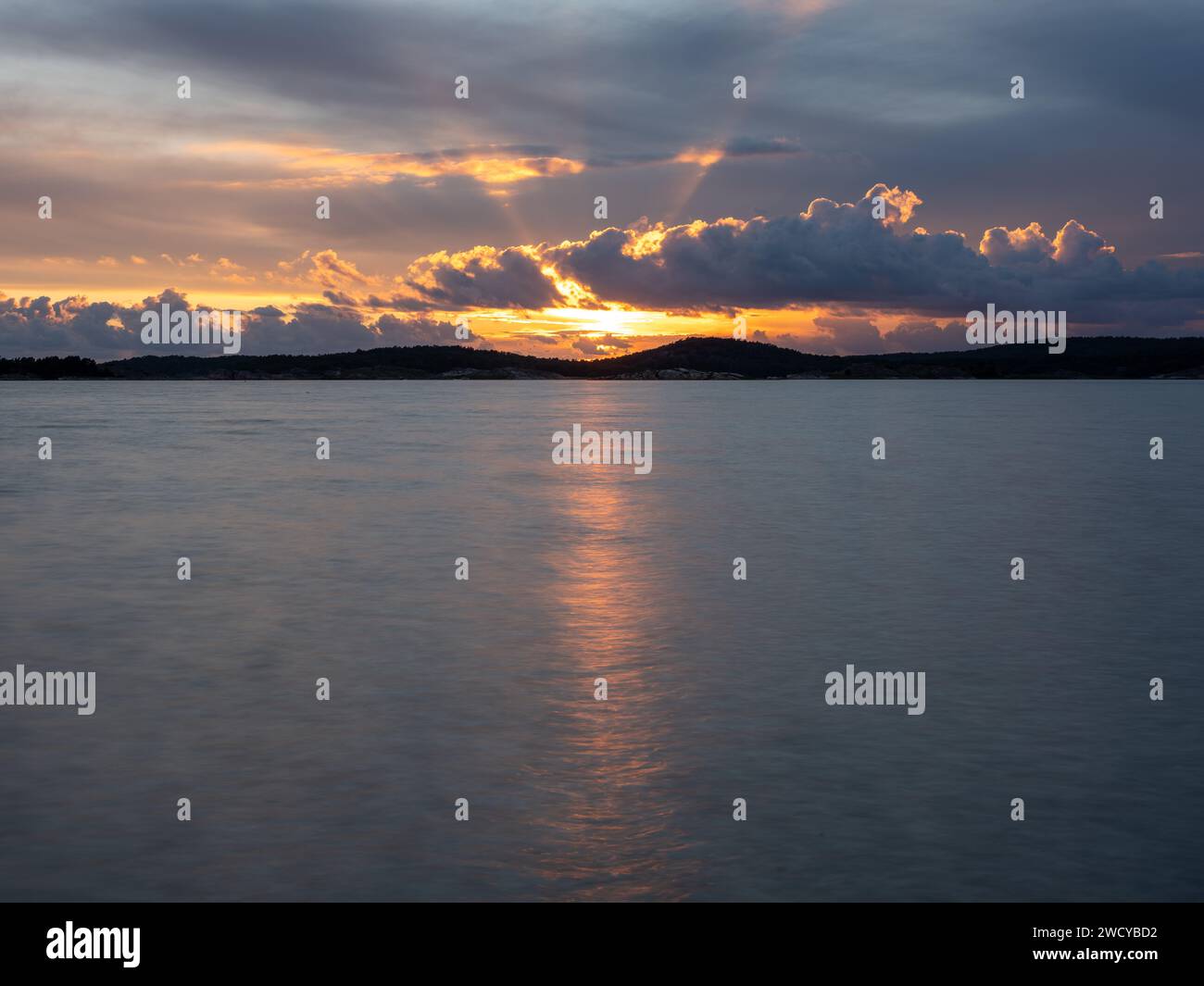 Nuvole e atmosfera in caldi colori serali con il sole dietro la luce nuvolosa che si riflette nel mare. Foto Stock
