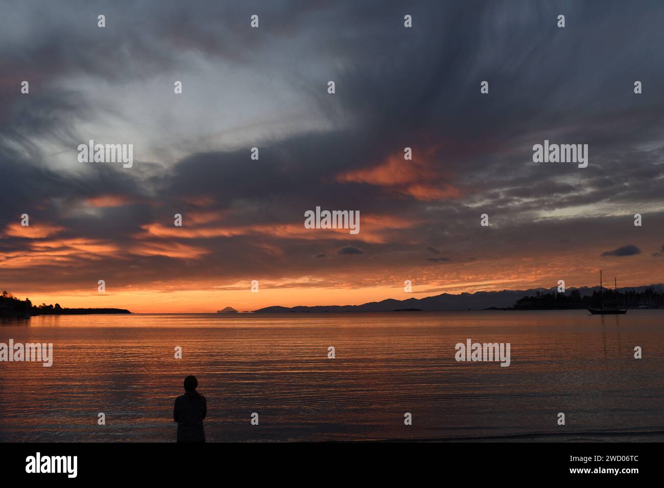 Una donna è sagomata mentre guarda il sole sorgere su una spiaggia sull'Isola di Vancouver, British Columbia, Canada. Foto Stock