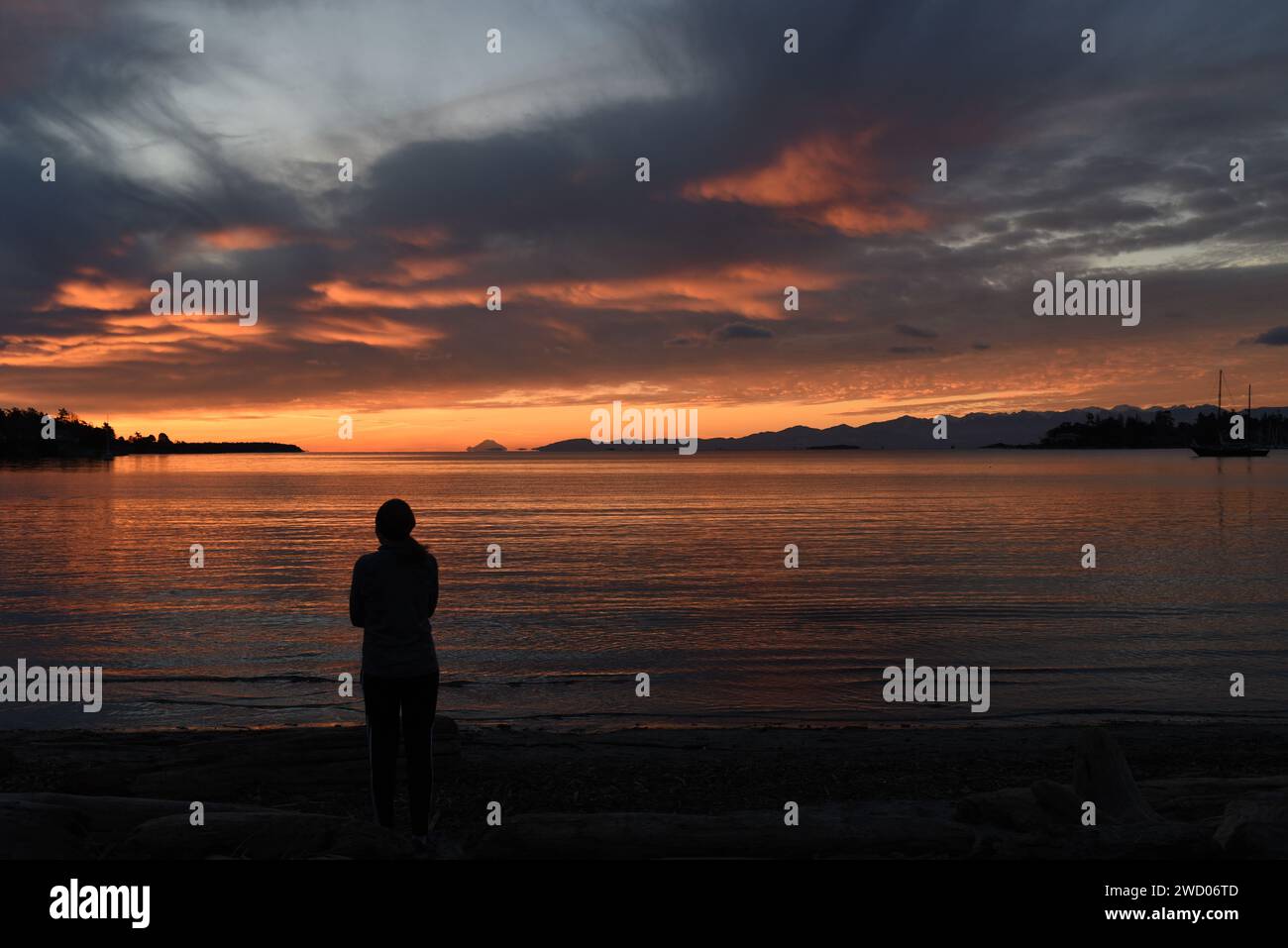Una donna è sagomata mentre guarda l'alba su una spiaggia sull'Isola di Vancouver, British Columbia, Canada. Foto Stock
