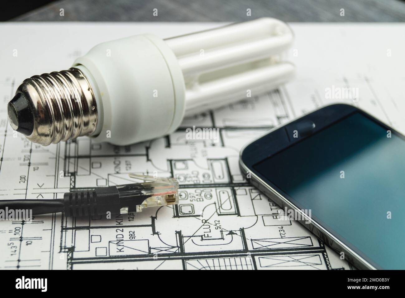 Lampada a risparmio energetico, smartphone e spina di rete sui disegni di costruzione, immagine simbolica per la casa intelligente Foto Stock