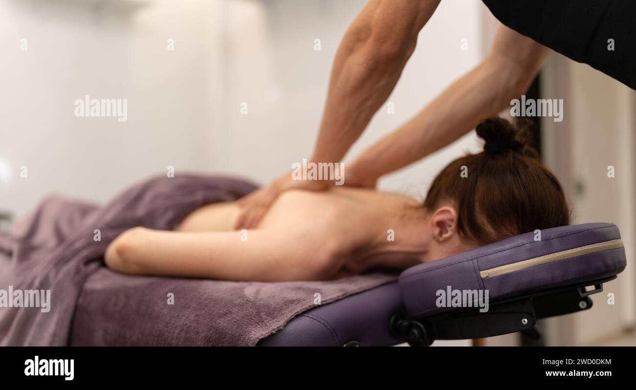 Una massaggiatrice professionale massaggierà con attenzione l'area delle spalle di una cliente bionda, garantendo un'esperienza rilassante. Foto Stock