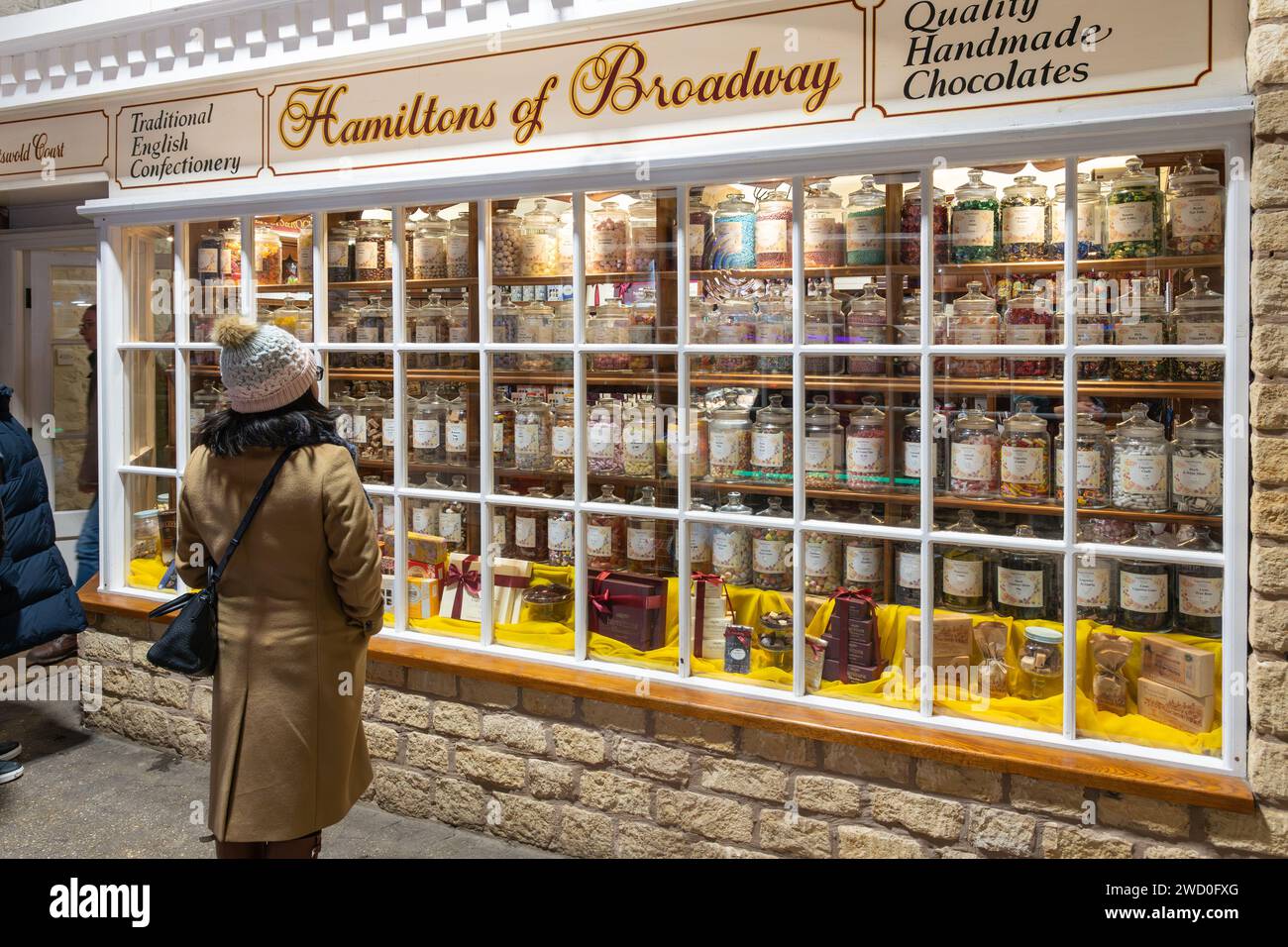Una donna che indossa un cappello da bobble in inverno che guarda alla finestra dell'Hamiltons di Broadway, un negozio di dolci con tradizionale pasticceria inglese. Inghilterra Foto Stock