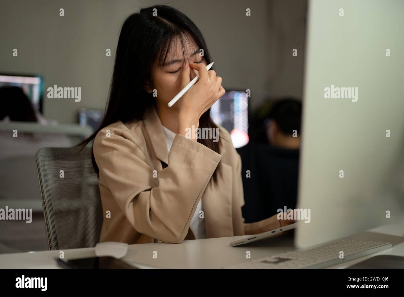Una giovane donna d'affari asiatica stanca e piena di lavoro o una dipendente d'ufficio soffre di affaticamento degli occhi mentre lavora al suo progetto su computer presso lui Foto Stock