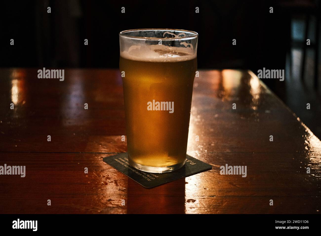 Una pinta di birra su un tavolo in una stanza buia Foto Stock