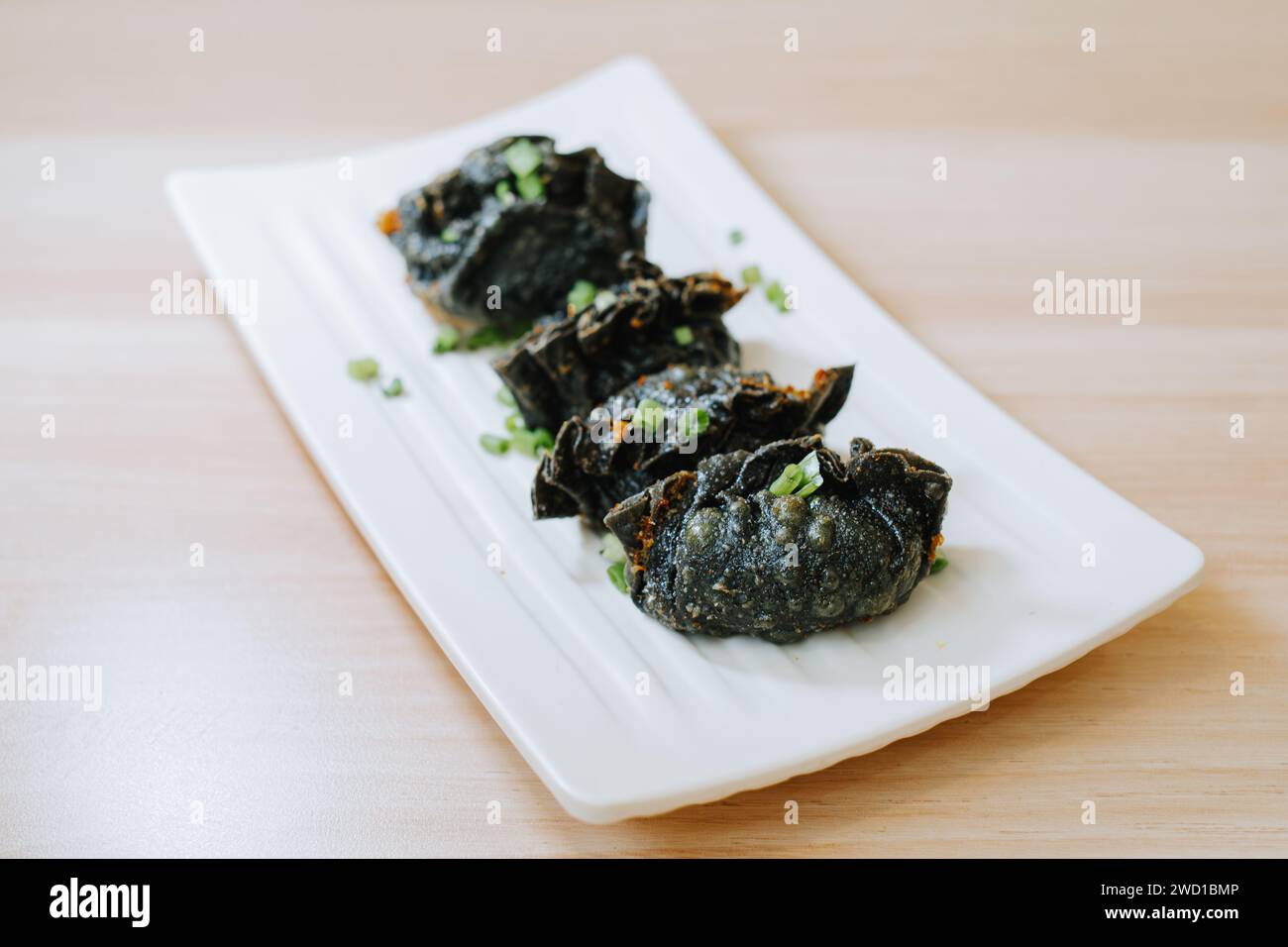 Black Fried Gyoza su un piatto su un tavolo di legno. Cibo di strada tradizionale giapponese. Foto Stock