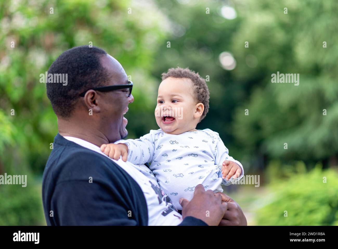 Padre coccola adorabile bambino birazziale, bambino afro-americano che guarda la macchina fotografica legarsi con papà all'aperto Foto Stock