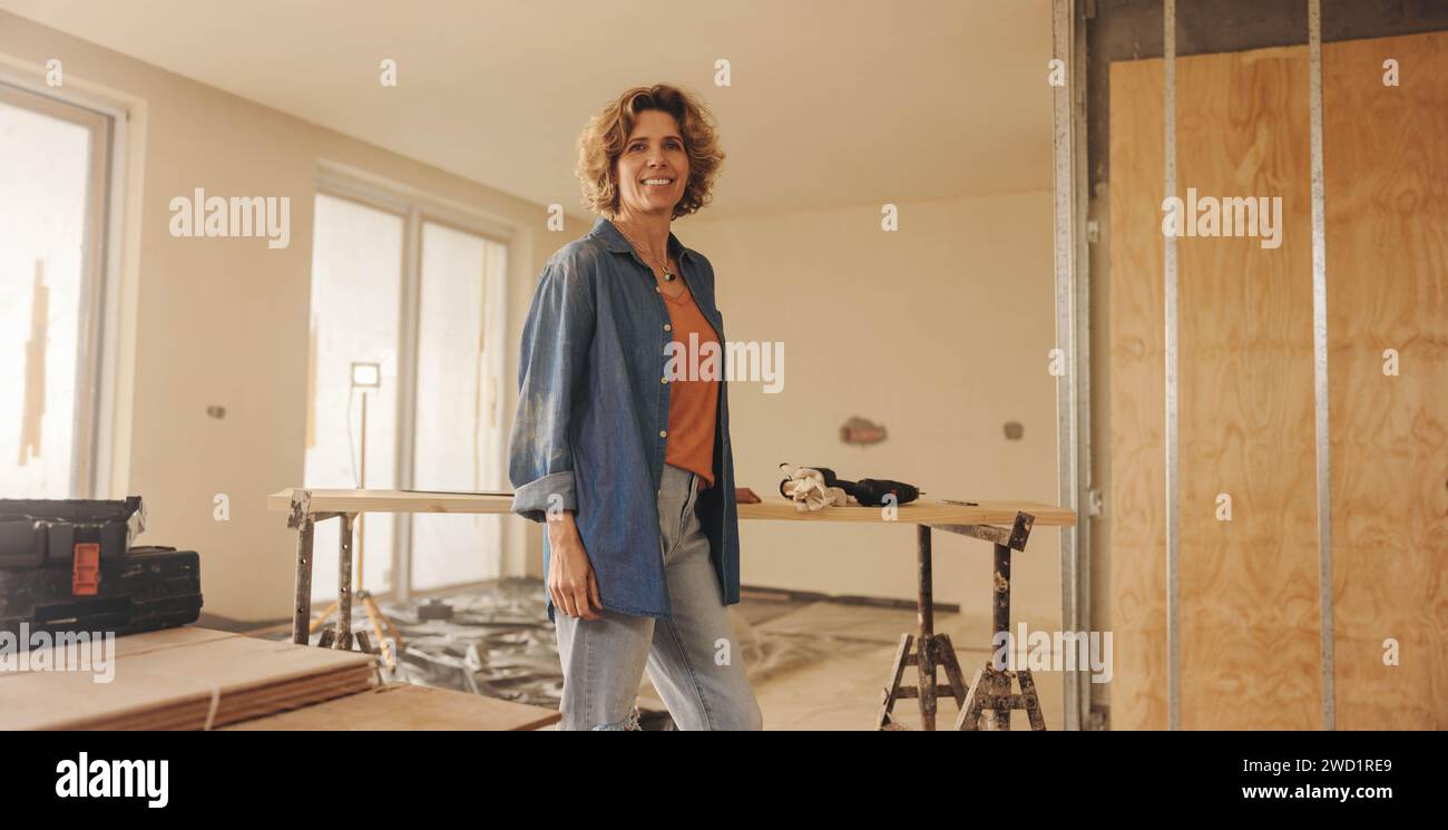 Donna matura in piedi nella sua cucina, rimodellando e ristrutturando con sicurezza la sua casa. Questo proprietario di casa è concentrato e determinato, creando una bella S Foto Stock