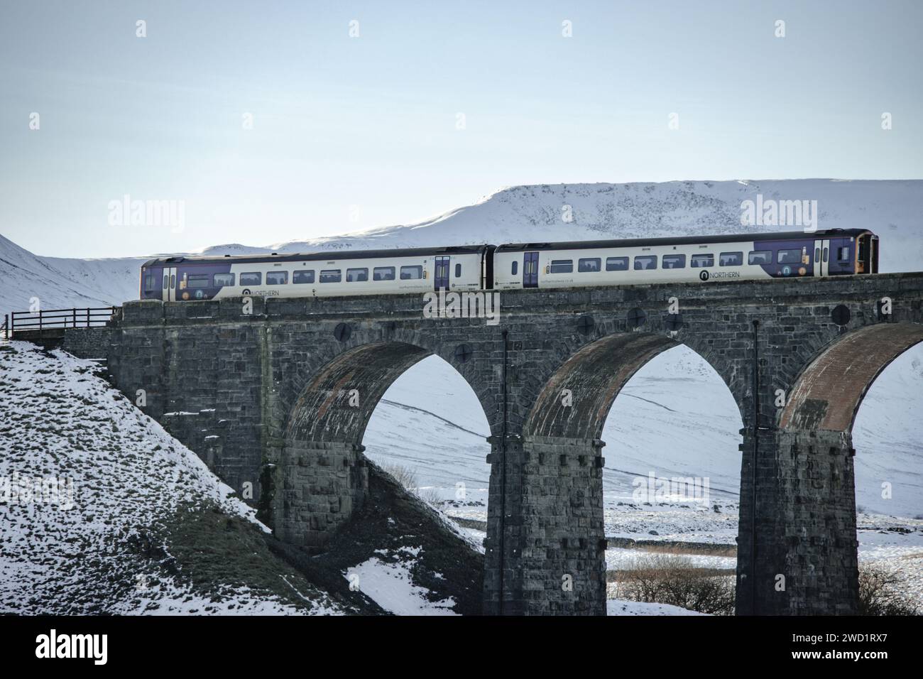 Un treno del nord che attraversa la ferrovia sul viadotto Ribblehead nella neve dello Yorkshire Dales National Park. Preso in una bella giornata di cielo blu. Foto Stock