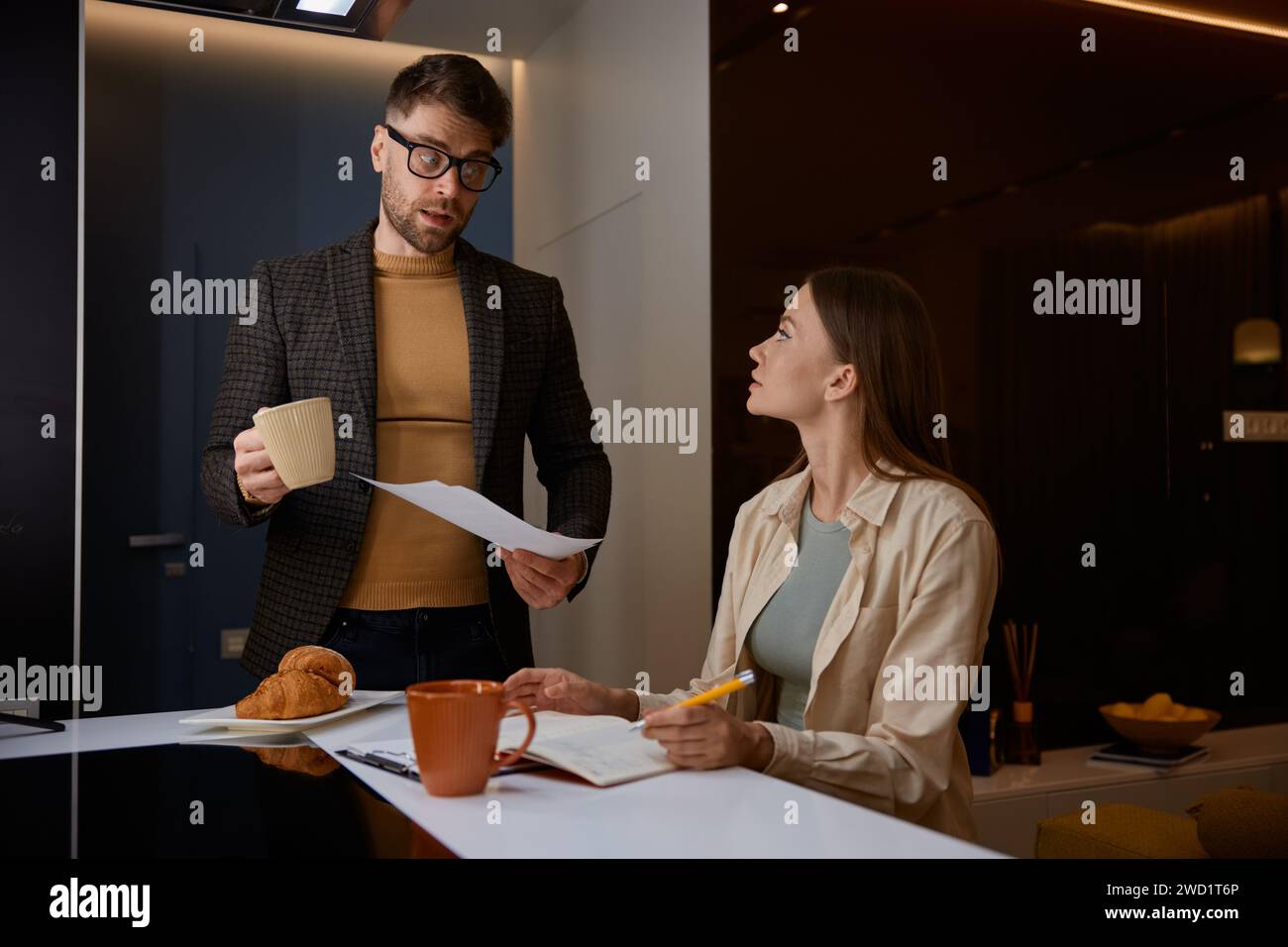 Un marito serio che tiene in mano la carta e chiede alla moglie dei costi aggiuntivi Foto Stock