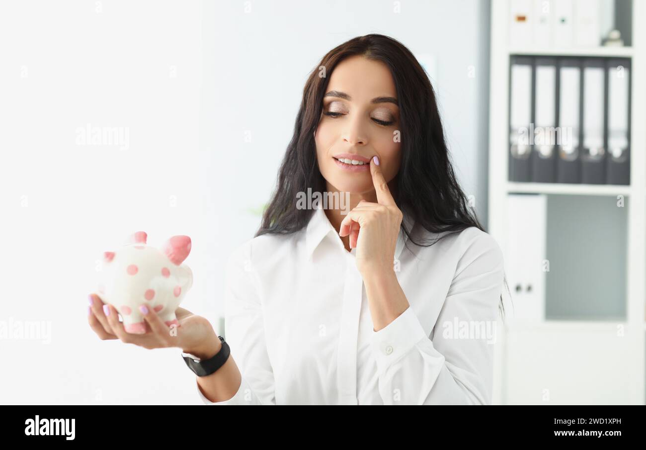 Donna tenere piggybank, pensare al modo migliore di utilizzare i soldi, risparmiare per il futuro Foto Stock