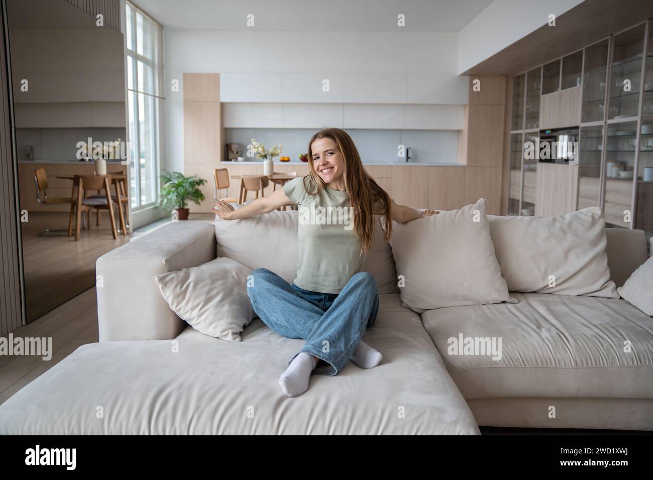 Donna bionda felice che si rilassa seduto sul divano guardando la macchina fotografica con un sorriso. Foto Stock