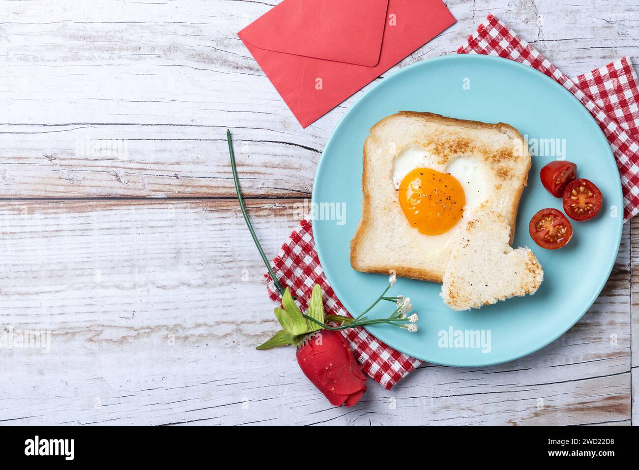 Colazione di San Valentino con uova con pomodori, pane a forma di cuore e pane tostato su un tavolo di legno Foto Stock