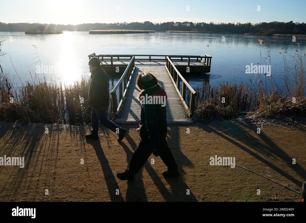 La gente passa davanti a uno stagno della flotta ghiacciata a Fleet, Hampshire. Il Regno Unito rimarrà in una situazione di freddo fino al fine settimana, con temperature di congelamento destinate a precipitare ulteriormente in gran parte del paese. Data foto: Giovedì 18 gennaio 2024. Foto Stock