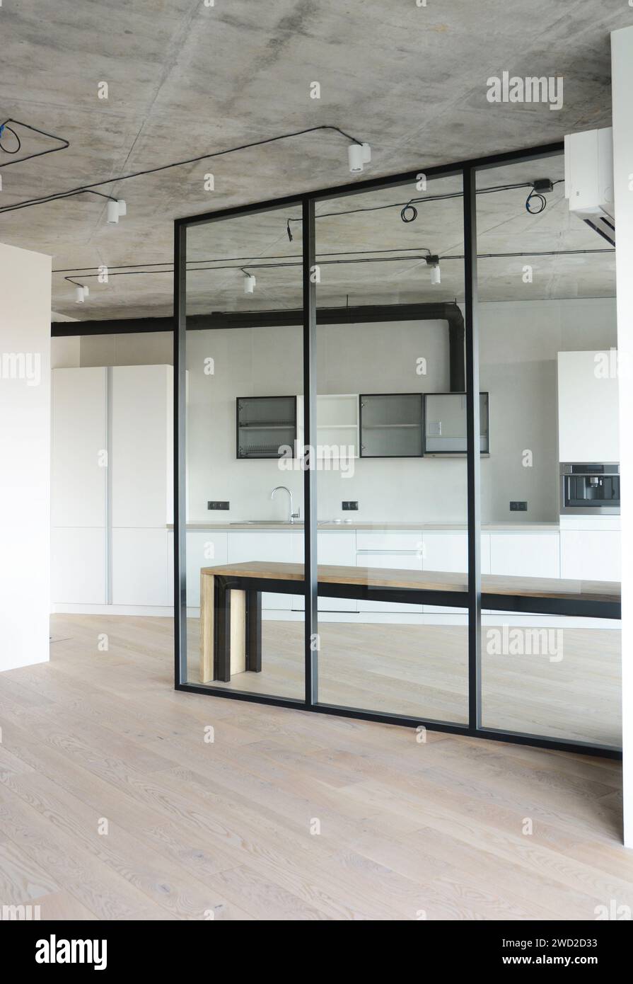 Monolocale bianco con pavimento in laminato di legno e parete divisoria in vetro che separa la cucina. Foto Stock