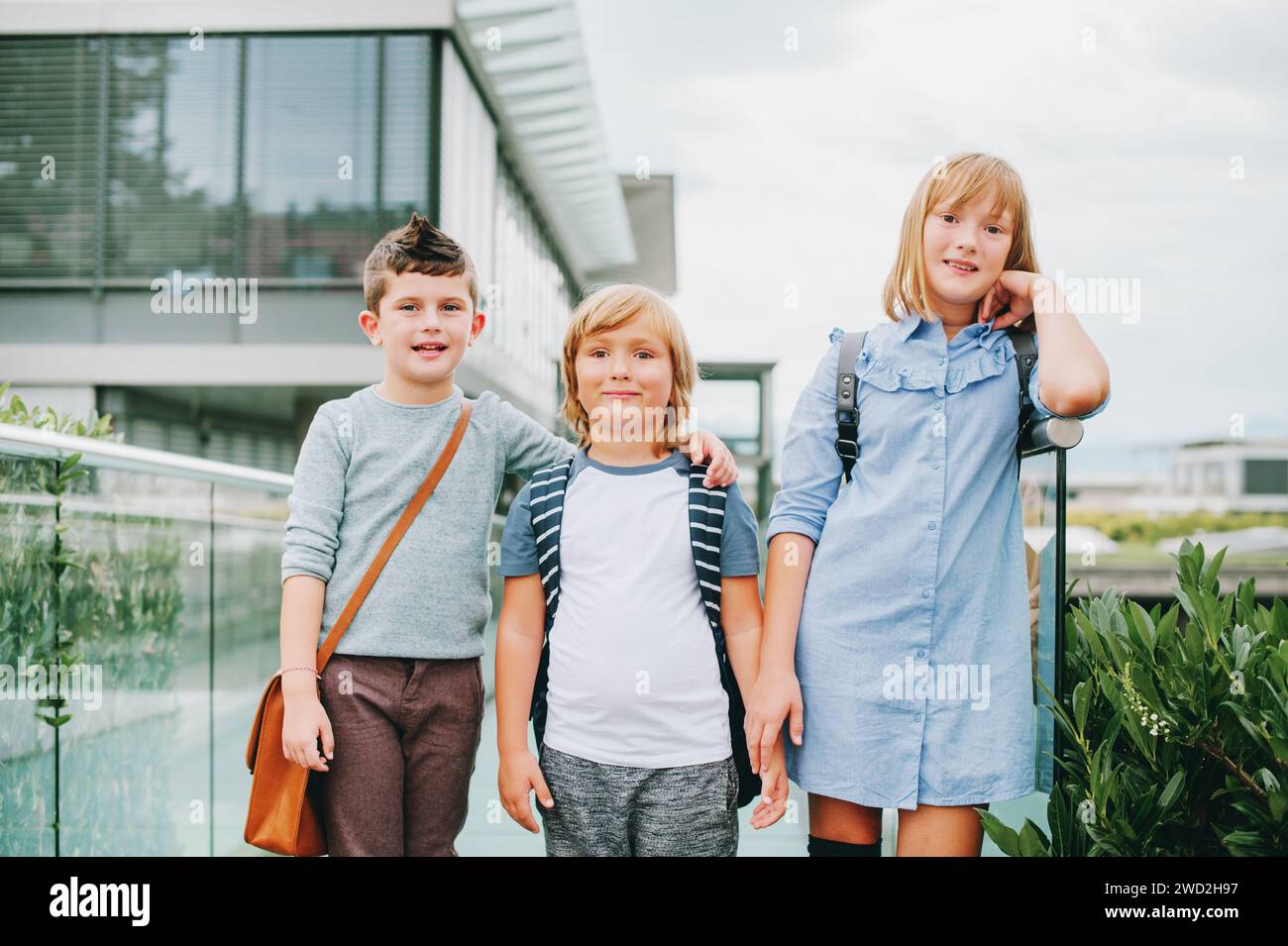 Gruppo di 3 simpatici scolari che fingono all'aperto e indossano zaini. Concetto di ritorno a scuola. Moda per bambini Foto Stock