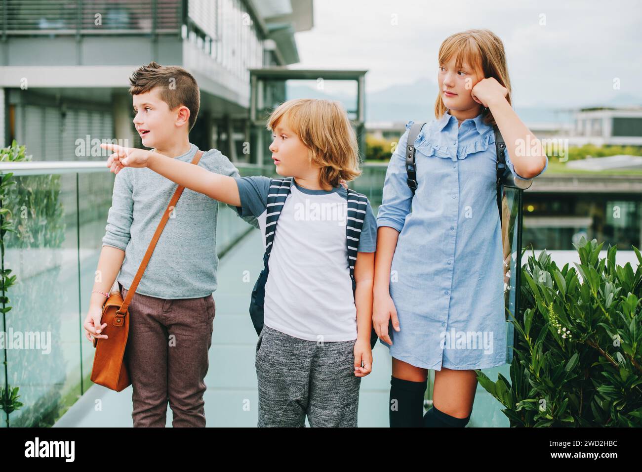 Gruppo di 3 simpatici scolari che fingono all'aperto e indossano zaini. Concetto di ritorno a scuola. Moda per bambini Foto Stock