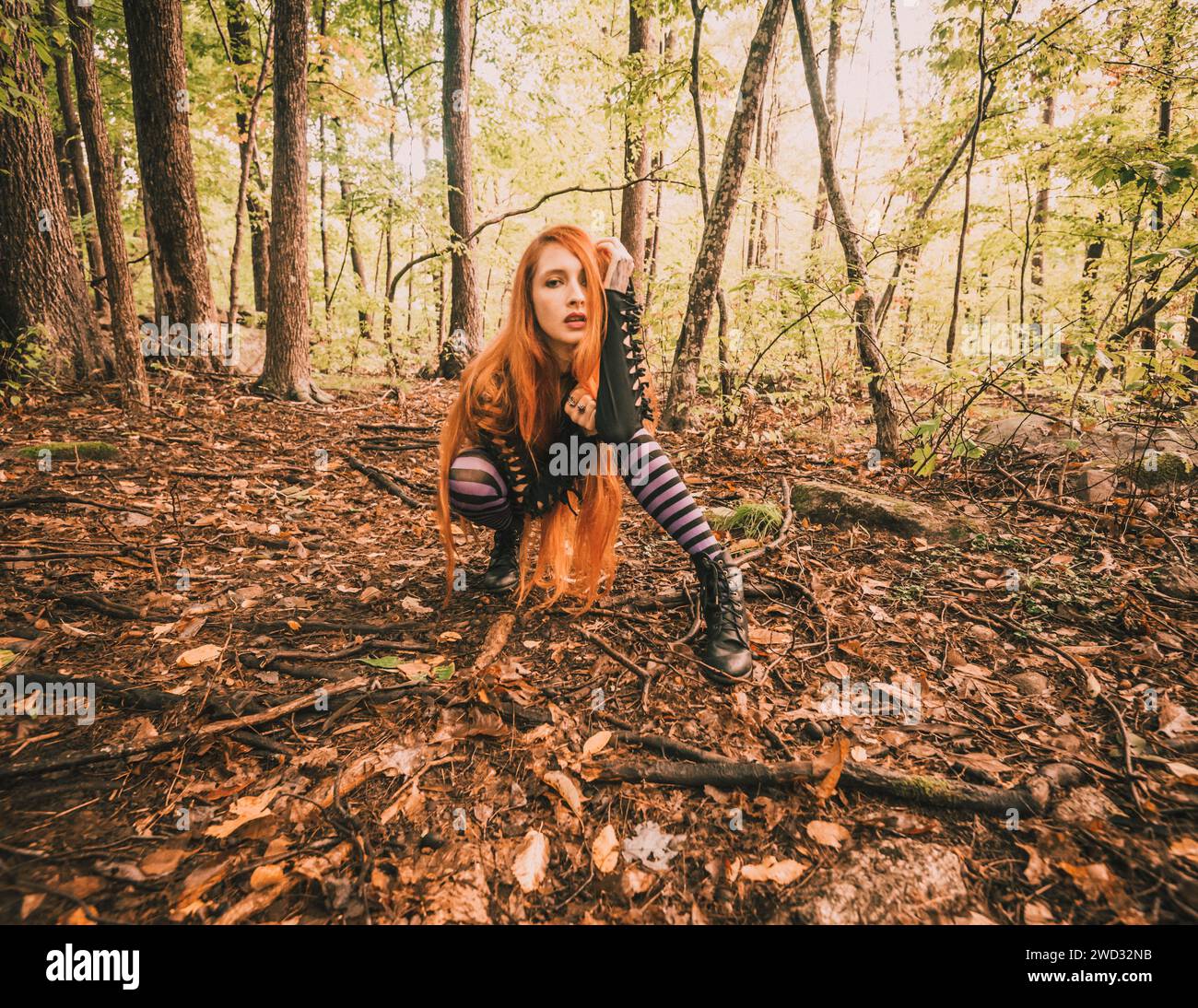 Una giovane donna dai capelli rossi con leggings a righe viola in posa nella foresta Foto Stock